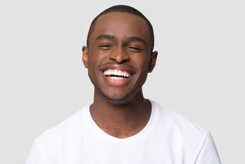 Cheerful happy african millennial man laughing looking at camera isolated on studio blank background, funny young black guy with healthy teeth beaming orthodontic white wide smile head shot portrait